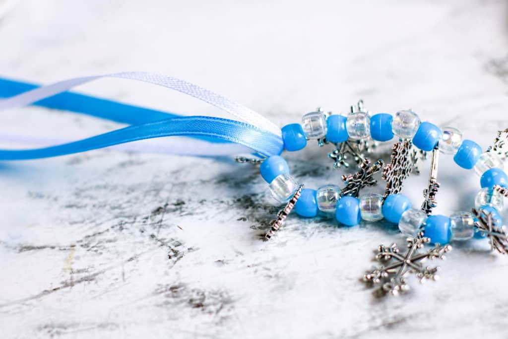 Cómo hacer una bella pulsera de cuentas y copos de nieve inspirada en la película Frozen, ideal para divertir a las princesas en casa.